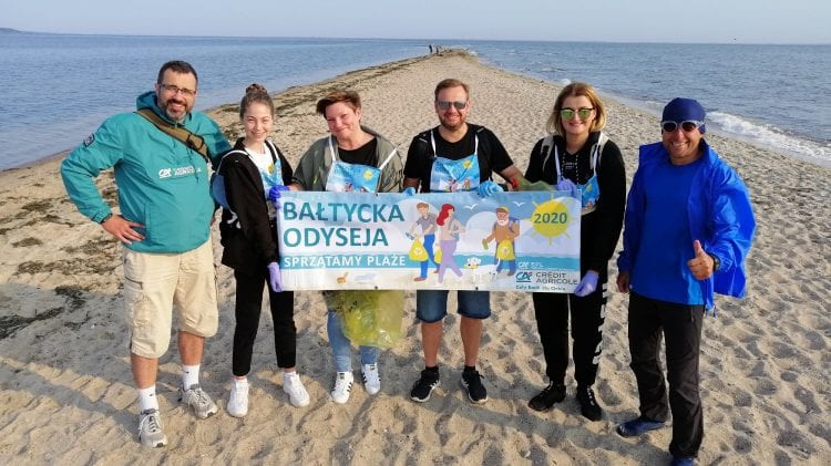 Grupa osób biorących udział w akcji ekologicznej na plaży w Polsce, trzymająca baner promujący Bałtycką Odyseję.