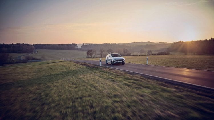 Biały samochód Hyundai jadący wiejską drogą o zachodzie słońca.