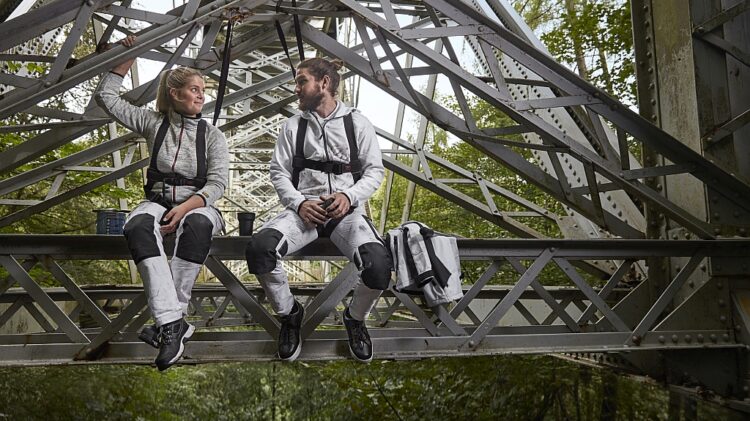 Dwie osoby ubrane w swobodne stroje siedzą na moście otoczonym bujnym lasem.