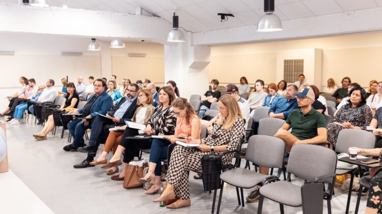 Grupa osób siedzących na krzesłach w sali podczas konkursu startupowego.