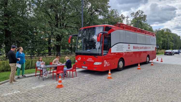         Czerwono-biały autobus zaparkowany na parkingu podczas akcji Krwi zbiórki sponsorowanej przez Credit Agricole.