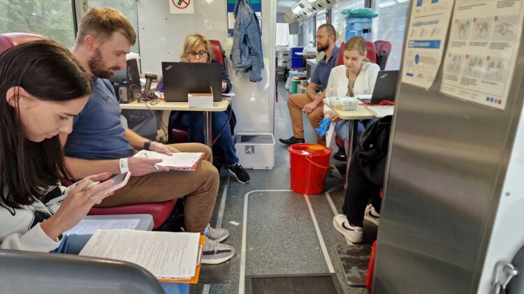 Grupa ludzi siedzących w pociągu i wpatrujących się w telefony podczas zbiórek.