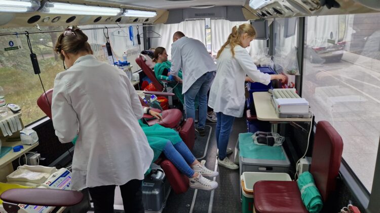 Grupa osób w białych fartuchach pracująca w autobusie podczas zbiórki na rzecz krwiodawstwa sponsorowanej przez Credit Agricole.