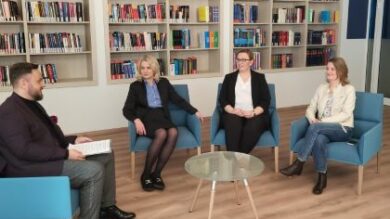 Grupa osób siedzących na krzesłach w pokoju z półkami na książki.