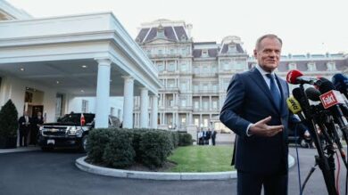 Mężczyzna w garniturze rozmawia z reporterami przed hotelem.