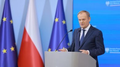 Mężczyzna wygłaszający przemówienie na podium, na tle Unii Europejskiej i polskich flag.