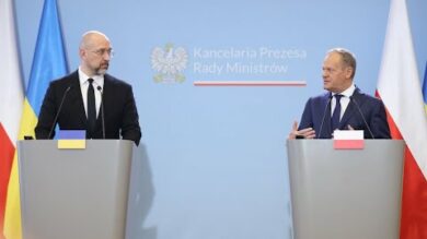 Dwóch urzędników stojących na podium z flagami Ukrainy i Polski, biorących udział w konferencji prasowej.