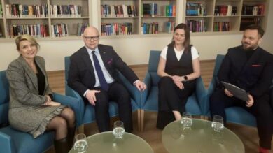 Czterech profesjonalistów siedzących w nowoczesnej przestrzeni biurowej z półką na książki w tle.