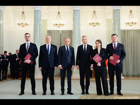 Pięciu urzędników stojących w formalnym rzędzie w eleganckiej sali, trzymających czerwone teczki podczas ceremonii.