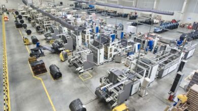 Przegląd dużej hali produkcyjnej z różnymi maszynami i pracownikami wykonującymi zadania.
