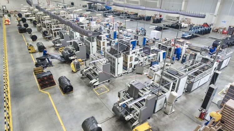 Przegląd dużej hali produkcyjnej z różnymi maszynami i pracownikami wykonującymi zadania.