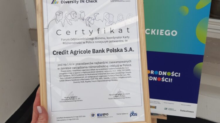 Certyfikat przyznany Credit Agricole Bank Polska S.A. doceniający wysiłki na rzecz różnorodności, zawieszony przed tablicą promującą miesiąc różnorodności „Miesiąc Różnorodności 2024.