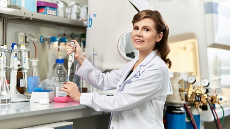 Kobieta w fartuchu laboratoryjnym używa pipety w warunkach laboratoryjnych. Na stole warsztatowym otacza ją sprzęt laboratoryjny i materiały eksploatacyjne.