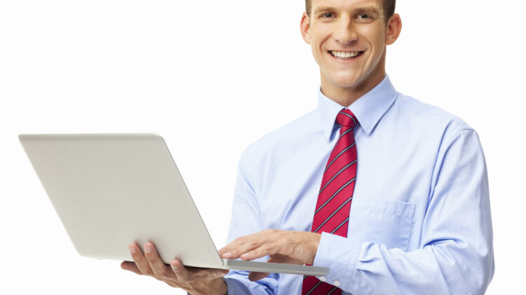 Uśmiechnięty biznesmen w niebieskiej koszuli i czerwonym krawacie, trzymający laptopa, stojący na białym tle.