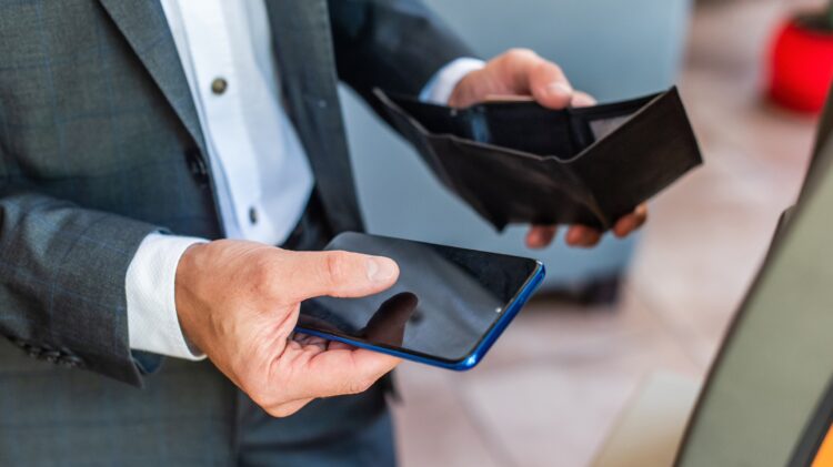 Mężczyzna w garniturze trzymający w jednej ręce pusty portfel, a w drugiej smartfon.