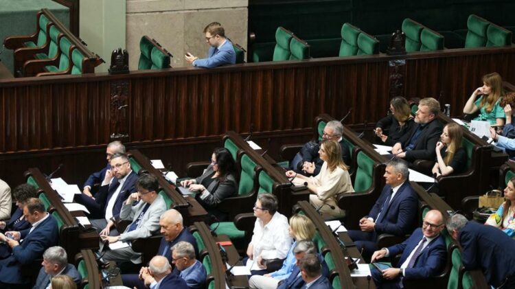 Grupa osób zasiadających w izbie ustawodawczej, przy czym niektóre osoby są zaangażowane w dyskusję, a inne robią notatki lub korzystają z urządzeń elektronicznych.