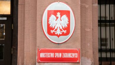Tablica z emblematem orła białego nad czerwoną tablicą z napisem „Ministerstwo Spraw Zagranicznych” na ścianie budynku.