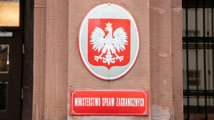 Tablica z emblematem orła białego nad czerwoną tablicą z napisem „Ministerstwo Spraw Zagranicznych” na ścianie budynku.