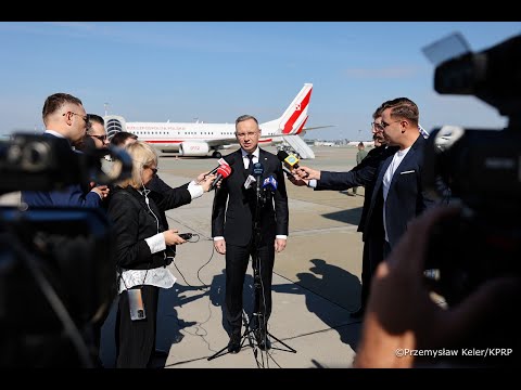 Mężczyzna w garniturze przemawia do wielu mikrofonów trzymanych przez reporterów na płycie lotniska, z samolotem w tle.