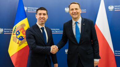 Dwóch mężczyzn w garniturach ściska sobie dłonie przed flagami Mołdawii i Polski. Stoją na niebieskim tle z napisem „Ministerstwo Spraw Zagranicznych.