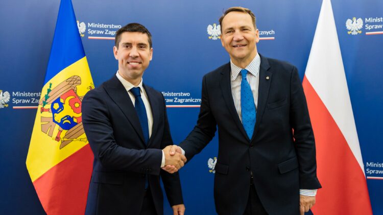 Dwóch mężczyzn w garniturach ściska sobie dłonie przed flagami Mołdawii i Polski. Stoją na niebieskim tle z napisem „Ministerstwo Spraw Zagranicznych.