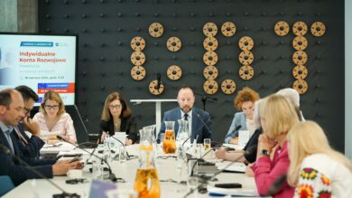 Grupa osób siedzących wokół stołu konferencyjnego w nowoczesnym biurze, zaangażowanych w spotkanie. Na ekranie prezentacji wyświetlane są informacje o webinarze inwestycyjnym.