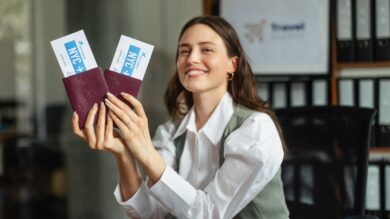 Kobieta siedząca przy biurku, uśmiechnięta i trzymająca dwa paszporty z kartami pokładowymi Nowego Jorku. W tle widoczny szyld biura podróży.