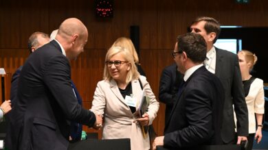 Grupa profesjonalistów w strojach formalnych stoi i rozmawia. Kobieta podaje rękę mężczyźnie, a inni patrzą i rozmawiają w tle.