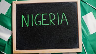 Tablica z napisem „Nigeria” w kolorze zielonym, na tle zielono-białych flag.